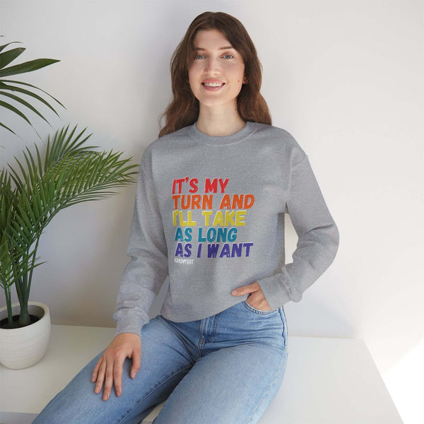 Woman wearing 'It's My Turn' unisex crewneck sweatshirt, gray, colorful text, casual style, sitting indoors, near a plant.