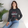 Woman wearing a 'Being a Grandma' unisex crewneck sweatshirt, sitting casually with plants in the background.