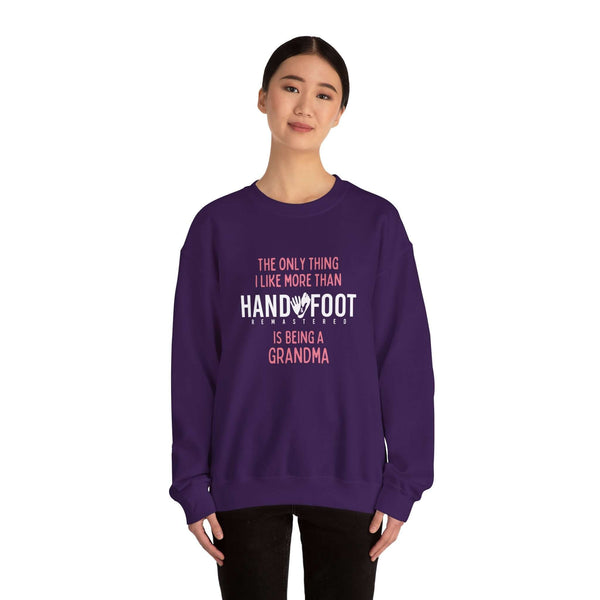 Woman wearing a purple crewneck sweatshirt with text 'The only thing I like more than hand and foot is being a grandma'.