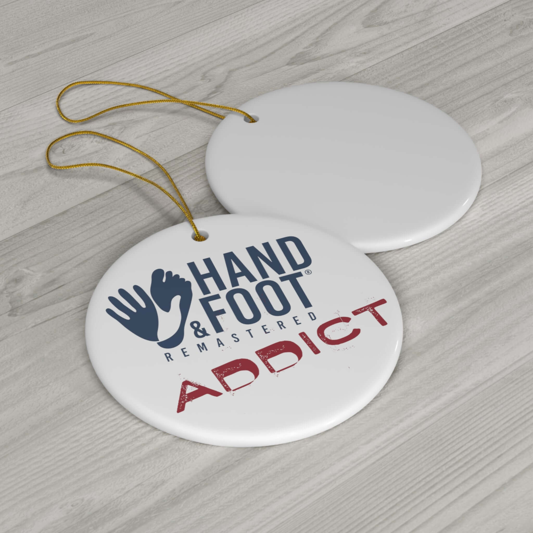 Hand & Foot Addict ceramic ornament with glossy finish and string, displayed on a wooden surface.