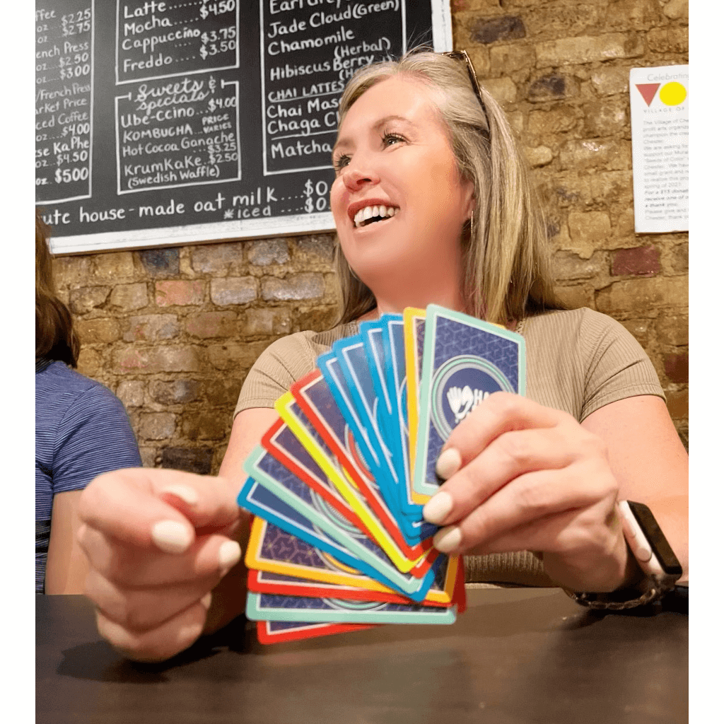 Woman smiling and holding colorful game cards while playing Scratch & Dent Hand & Foot Remastered.