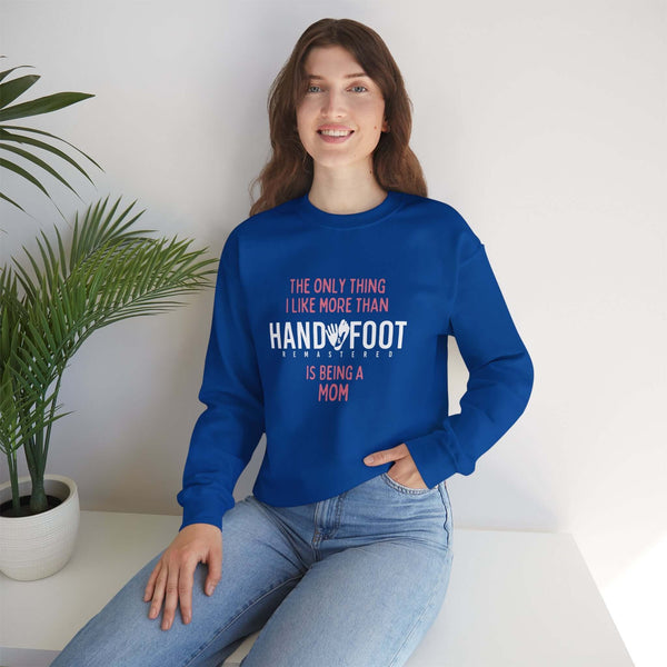 Woman wearing blue sweatshirt reading 'The Only Thing I Like More Than Hand & Foot is Being a Mom', sitting on a couch with a plant.