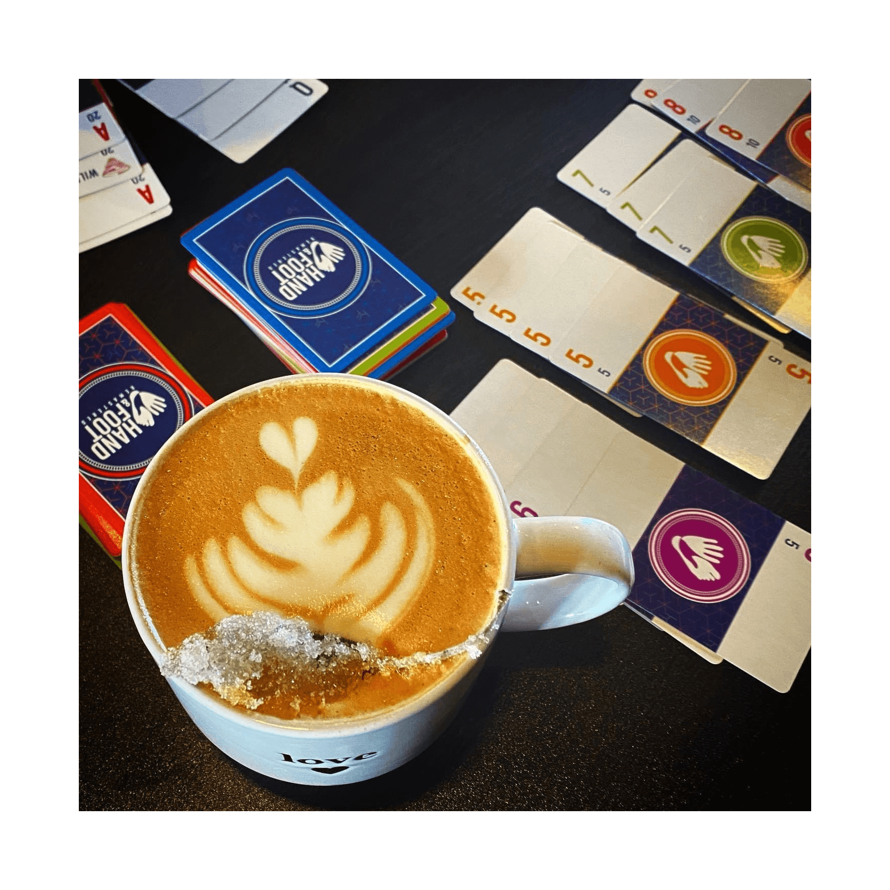 Top view of latte art in a mug next to colorful card game sets on a table.