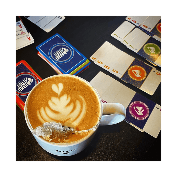 Top view of latte art in a mug next to colorful card game sets on a table.