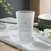 Tears of the People I Beat 16 oz Frosted Pint Glass on a table with floral accents, perfect for competitive gatherings.
