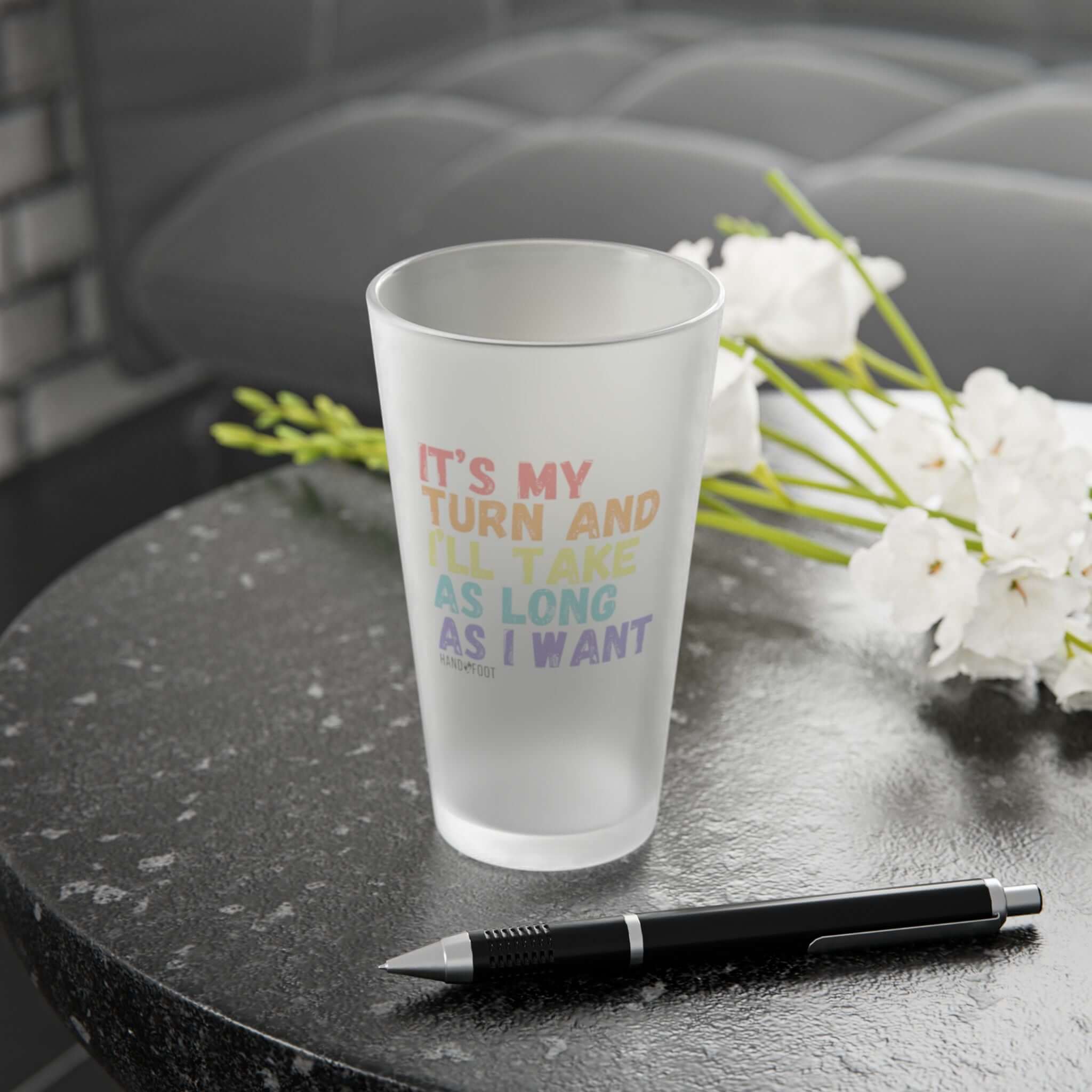 It's My Turn 16 oz Frosted Pint Glass on table with flowers, ideal for gifts or gatherings. Fun design enhances drinkware collections.