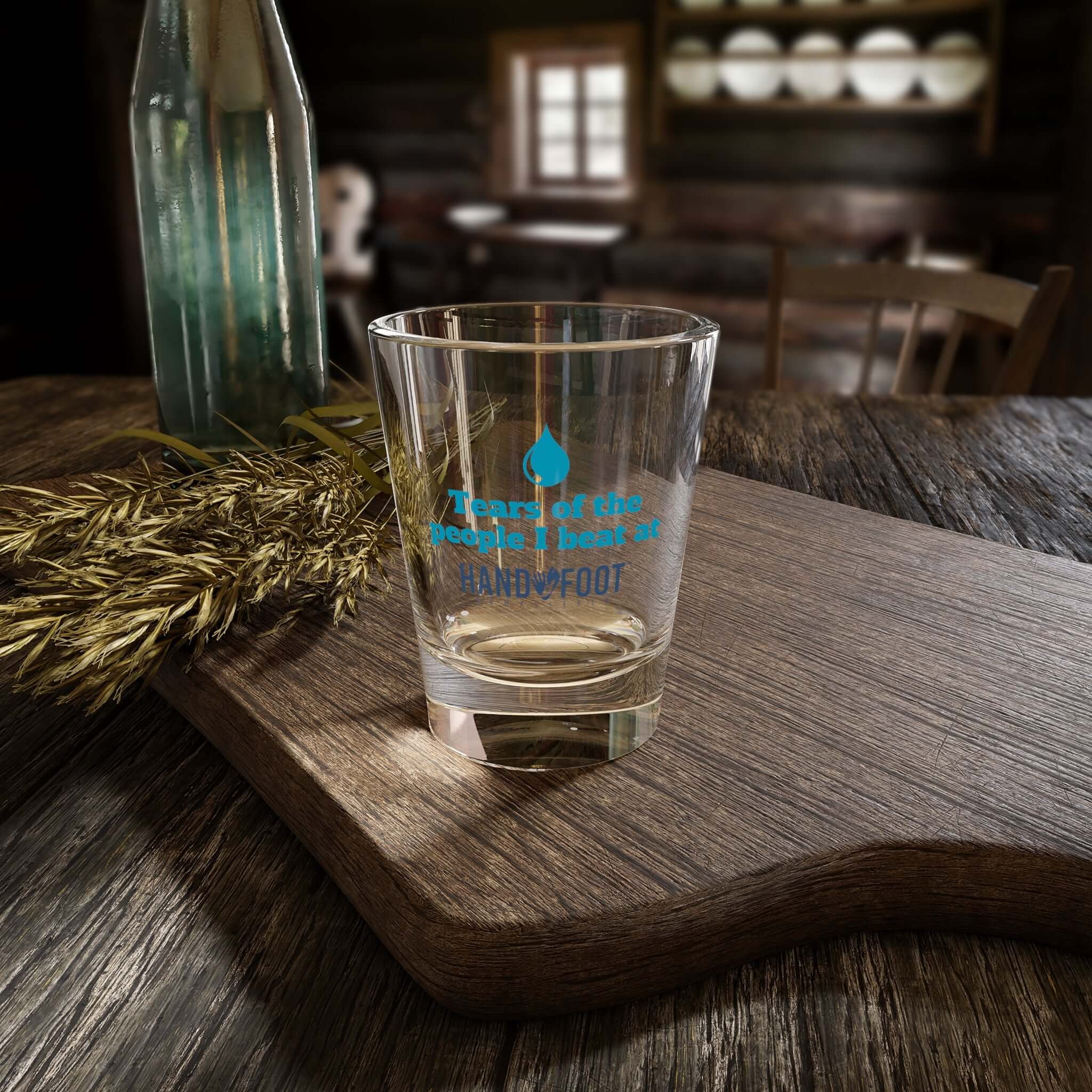 Shot glass with 'Tears of the People I Beat' text, ideal for parties and collections, sitting on a rustic wooden table.